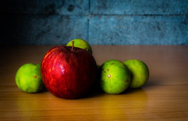 Kırmızı elma ve limon dramatik aydınlatma, ahşap bir masa üzerinde seçici odak.