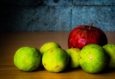 Kırmızı elma ve limon dramatik aydınlatma, ahşap bir masa üzerinde seçici odak.