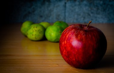 Kırmızı elma ve limon dramatik aydınlatma, ahşap bir masa üzerinde seçici odak.