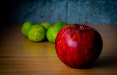 Kırmızı elma ve limon dramatik aydınlatma, ahşap bir masa üzerinde seçici odak.