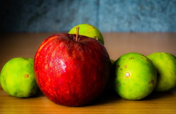 Kırmızı elma ve limon dramatik aydınlatma, ahşap bir masa üzerinde seçici odak.