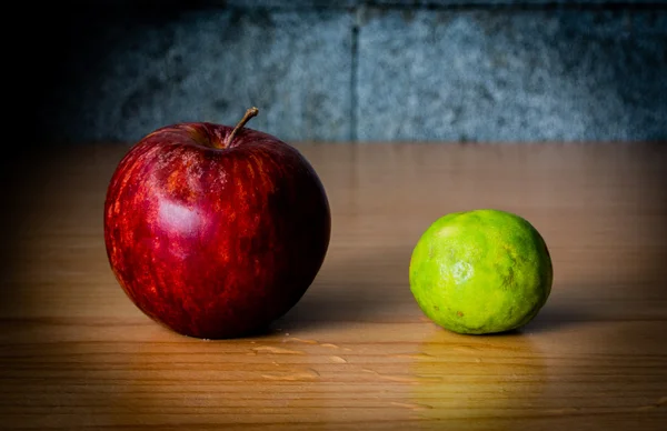 Kırmızı elma ve limon dramatik aydınlatma, ahşap bir masa üzerinde seçici odak.