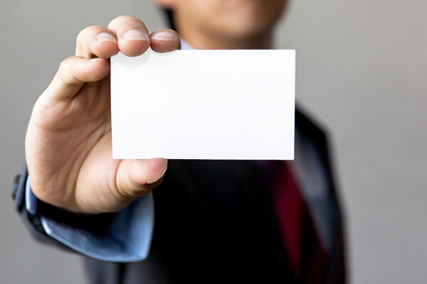 Young man in business suit holding white blank business card.