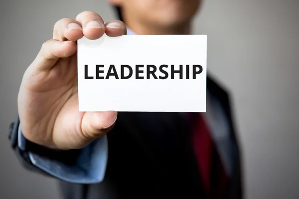 Üzletember bemutatja a "Leadership" szó, fehér karton — Stock Fotó