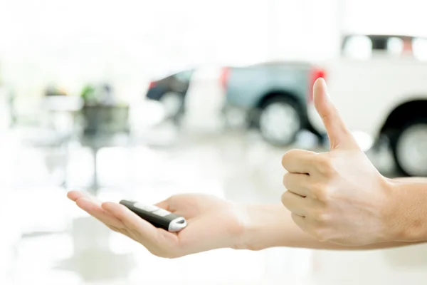 Ανθρώπινα χέρια δίνοντας τους αντίχειρες επάνω με αυτοκίνητο κλειδί στο shoowroom αυτοκινήτων — Φωτογραφία Αρχείου