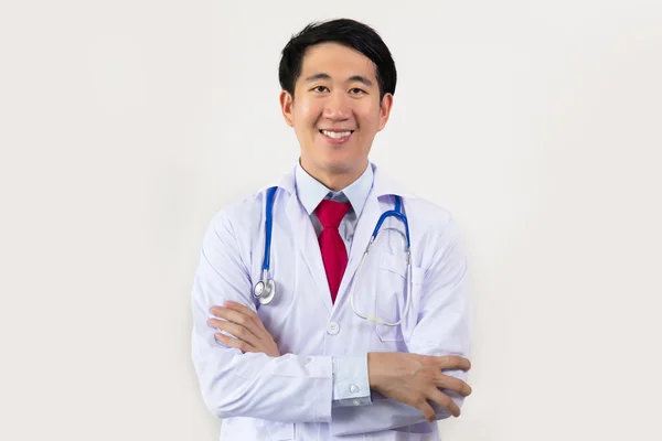 Νεαρά ασιατικές αρσενικό ο γιατρός, χαμογελώντας με τα χέρια διπλωμένα έχοντας στηθοσκόπιο στο λαιμό του απομονώνονται σε λευκό φόντο — Φωτογραφία Αρχείου