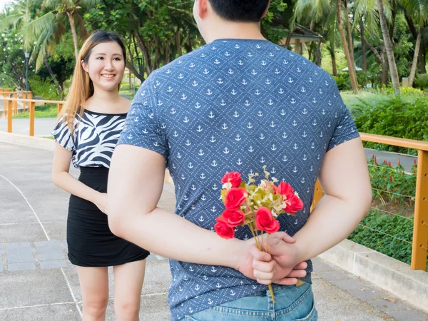 Молодой человек прячет розы от спины и дарит их своей девушке . — стоковое фото