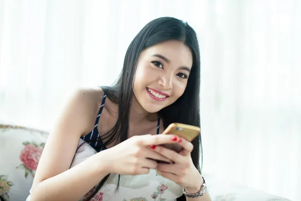 Азиатка играет на своем телефоне на уютном диване — стоковое фото