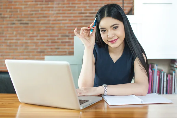 Asian Woman Thinking and Smiling at camera in modern office