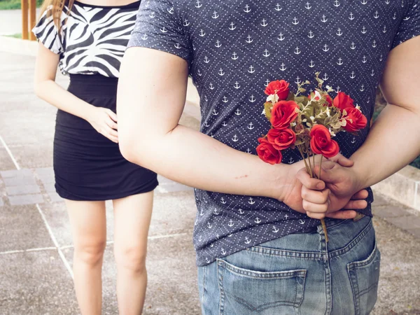 Молодой человек прячет розы от спины и дарит их своей девушке . — стоковое фото