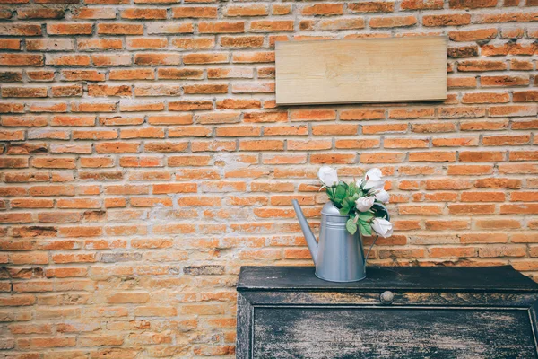 Hermoso florero de flores en armario envejecido en fondo de pared de ladrillo vintage rojo con letrero de tablero de madera vacío . —  Fotos de Stock