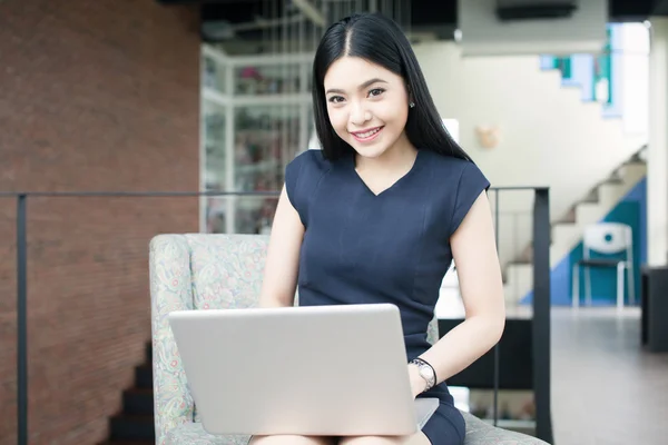 Asiática mujer sentado y jugando un portátil en oficina fondo — Foto de Stock