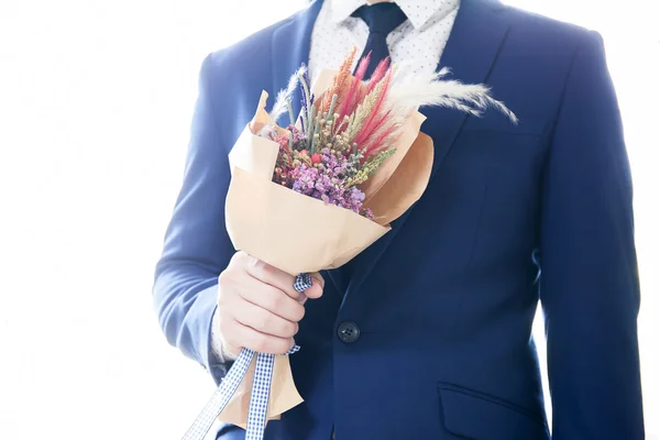Homme en costume tenant bouquet avec la lumière de jante blanche de fond . — Photo
