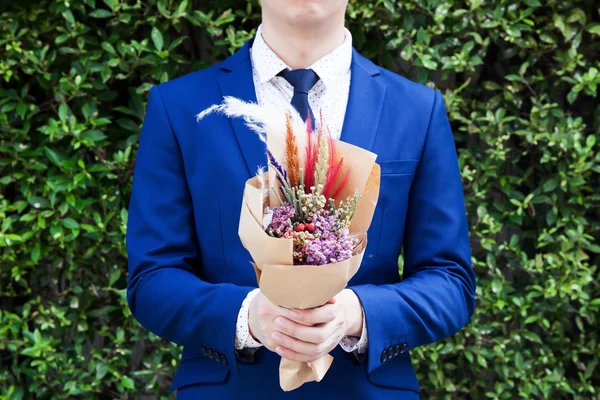 Giovane uomo in abito alla moda che tiene bouquet fatto a mano hipster — Foto Stock