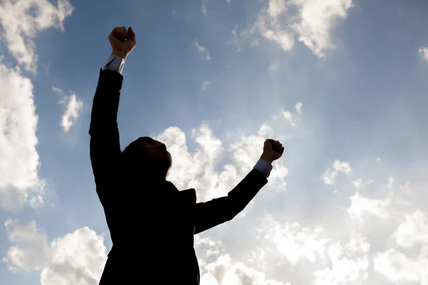 Silhouette of happy businessman raising arms up against blue sky Royalty Free Stock Images