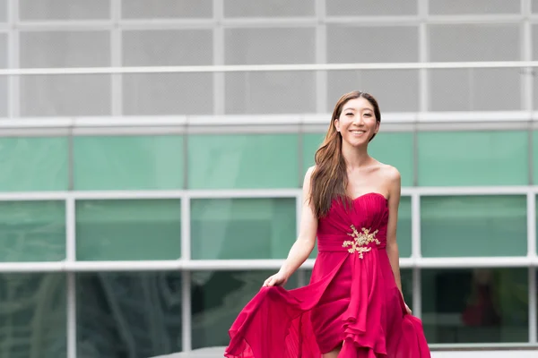 Heureuse et souriante femme asiatique mignonne marchant en robe de soirée rouge — Photo