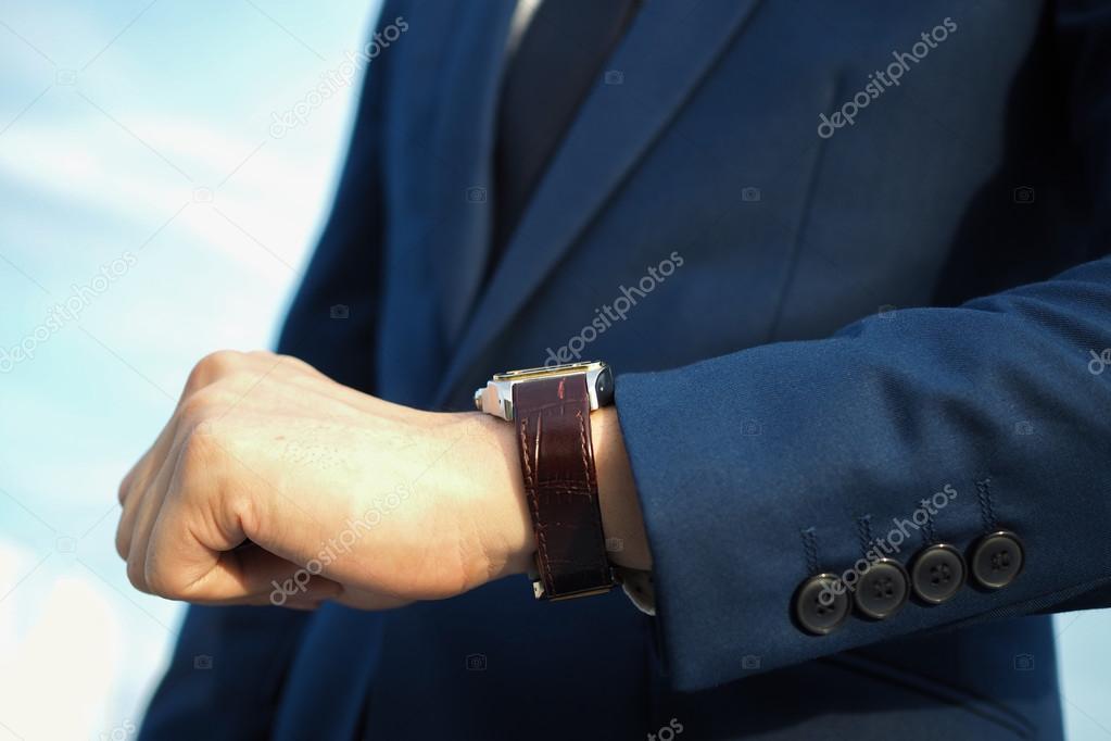 Fashionable businessman in elegant blue suit looking at luxury watch and waiting.