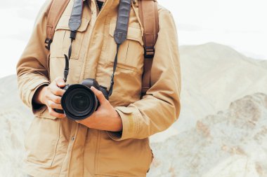 Seyahat fotoğrafçı gazeteci bir dslr fotoğraf makinesi dağ arka planda tutan Close-Up.