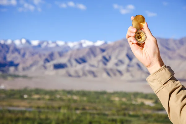 Young traveler looking at compass in Himalaya mountain view background (Focus on compass)