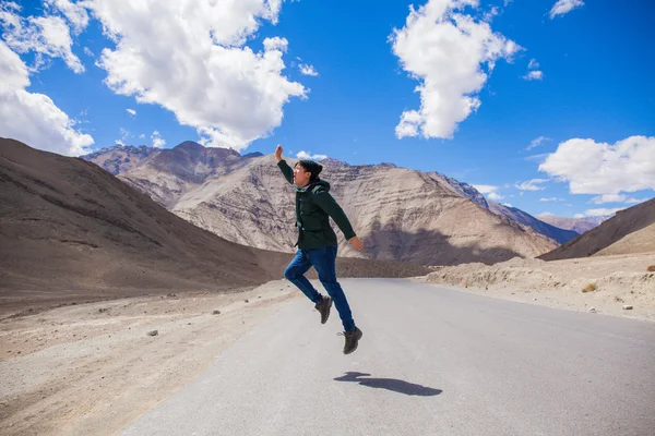 Extremely happy young male tourist jumping on country road with giant mountains behind — Stock Photo, Image
