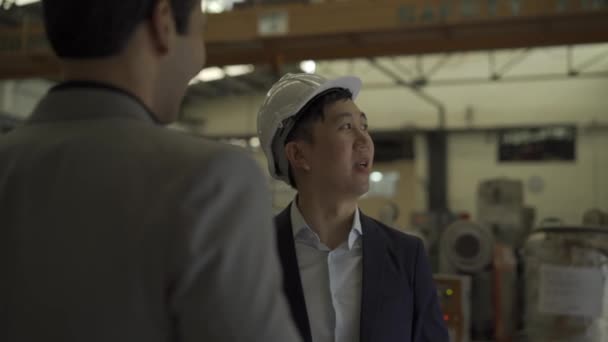30 'lu yaşlarda, resmi takım elbiseli Asyalı genç bir işadamı ve iş ortağıyla tokalaşan endüstriyel bir şapka. İş ortaklığı ve takım çalışması başarı kavramı — Stok video
