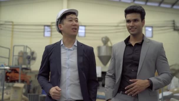 Zwei junge erwachsene Geschäftsleute unterhalten sich beim Gang in die Fabrik. Asiatische und indische Männer im Business-Anzug reden miteinander. — Stockvideo
