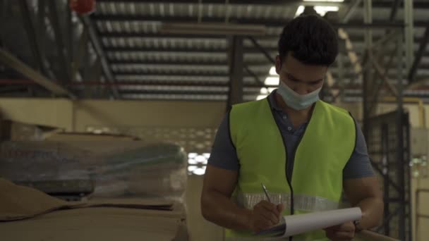 Mladý indický skladník v továrně nosí během práce ochrannou masku a bezpečnostní přilbu. 30s muž kontrolu zásob během Coronavirus Covid 19 pandemie — Stock video