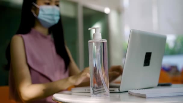 Korumacı Covid-19 yüz maskesi takan Asyalı iş kadını modern ofiste çalışıyor ve bilgisayar, koruma, sağlık kullanarak alkol jeli için bastırıyor. Yeni normal çalışma hayatı. — Stok video