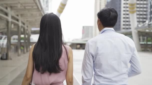 Jóvenes empresarios asiáticos usando un teléfono móvil y discutiendo mientras caminan cerca de edificios de oficinas. Atractiva mujer de negocios y hombre de Asia hablando - 4K alta calidad de imágenes — Vídeos de Stock