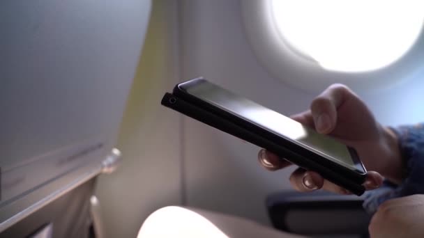 Młody, dorosły turysta trzymający komórkę w kabinie samolotu. Technologia bezprzewodowa i połączenie na pokładzie — Wideo stockowe