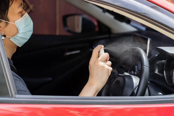 Asiatisk man i ansiktsmask med alkoholspray för att desinficera ratten i bilen. Sprutning förebygger infektion av coronavirus Covid-19 — Stockfoto