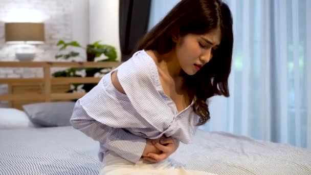Porträtt av 20-talets unga asiatiska kvinna som lider av smärta och värk som orsakas inne i magen i ett sovrum på natten. Symtom som diarré, förstoppning, tarm, gastrit, menstruation — Stockvideo