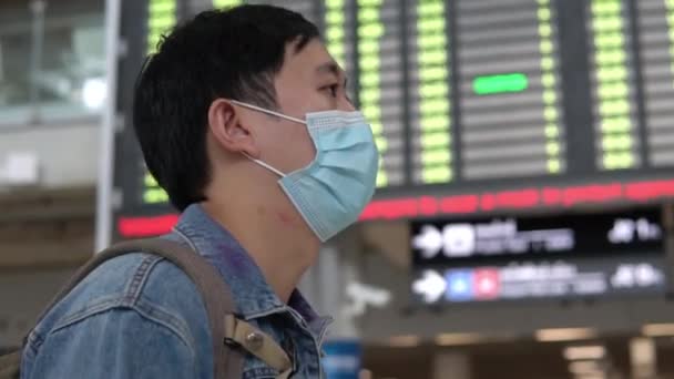 Азіатський чоловік подорожує в масці, чекаючи на літак. Молоді туристи ходять в аеропорту з посадкою на задньому плані під час пандемії Ковід-19. — стокове відео
