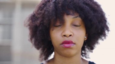 Afro saçlı genç Afrikalı Amerikalı kadın kameraya bakıyor ve çatılara gülümsüyor. Mutlu ve kendine güveni tam bir siyahi kadının aşırı yakın plan yüzü.