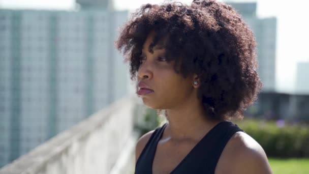 Joven mujer afroamericana mirando a lo lejos en los edificios del horizonte en los tejados. Atleta femenina determinada en atuendo deportivo con espacio de copia — Vídeos de Stock