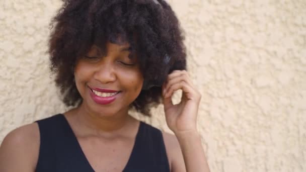 Jovem afro-americana em penteado afro com fones de ouvido na rua. Cantora negra feminina ouvindo o som da música com felicidade. — Vídeo de Stock