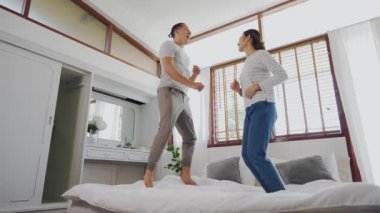 Portre mutlu, genç, Asyalı bir çift yatak odasının iç sahnesinde birlikte yatağa atlıyor. 30 'ların karı ve kocaları gülümsüyor ve el ele tutuşuyorlar. Evlilik ve mutlu ilişki hayatı kavramı