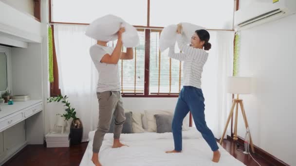 Unga vuxna asiatiska par spelar kuddkrig i sovrummet inredningsscen. 30-talets mogna man och hustru ler och har en rolig aktivitet. Äktenskap och lyckligt förhållande — Stockvideo