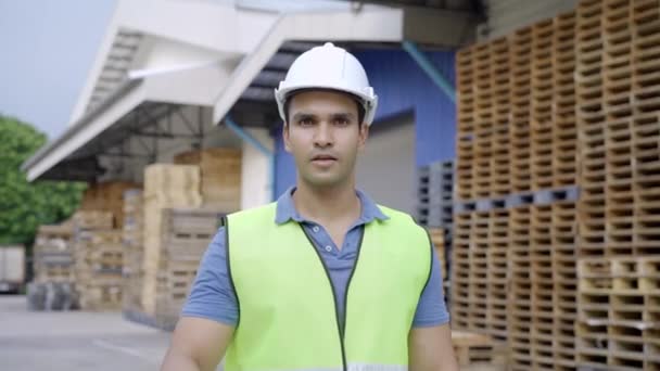 カメラと笑顔を見て20年代幸せなインドの流通倉庫デポ労働者。運送物流会社でのハードヘルメットで陽気で自信のある男性労働者は親指を放棄 — ストック動画