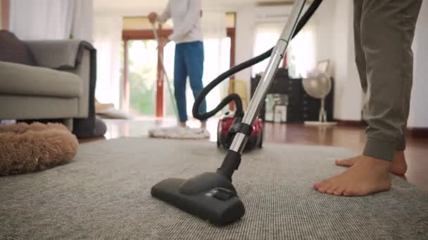 Glückliches junges Paar putzt Teppich mit Staubsaugermaschine und Mann wischt im modernen Zuhause den Boden — Stockvideo