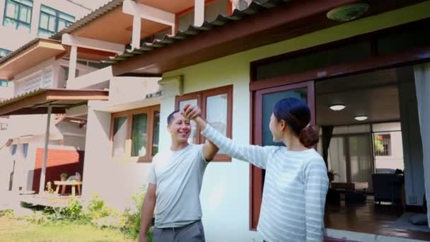 Mladý dospělý asijský pár drží ruce nahoru spolu s domácím interiérem v pozadí. Šťastný, dospělý muž a žena se usmívají. Koncepce nemovitostí a nemovitostí — Stock video