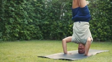 Evin bahçesinde bacak açıcı yoga pozu pratiği yapan genç bir adam. Kafkas erkek yoga öğretmeni amuda kalkarken parkta egzersiz yapıyor ve esniyor.