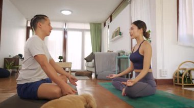 Genç adam evde özel eğitmenle yoga yapıyor. Erkek öğrenci yoga pozu vermek için kadın antrenörü takip ediyor.
