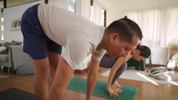 Mladý pár cvičí jógu na pozdrav slunci doma. Asijské žena a kavkazský muž cvičení a strečink v obývacím pokoji uvnitř — Stock video