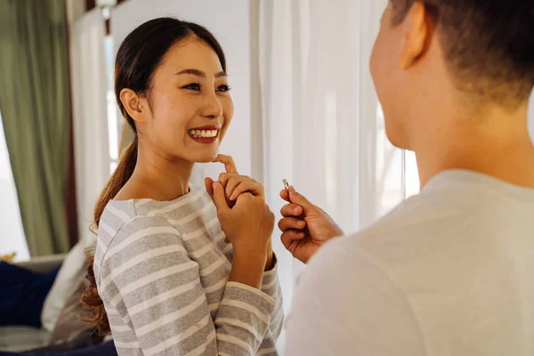 Unge man friar till sin flickvän med ring hemma. Asiatisk kvinna blir överraskad av sin pojkvän med frieri — Stockfoto