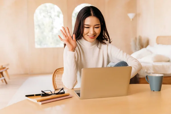 Genç Asyalı kadın, yatak odasında dizüstü bilgisayarında birine gülümseyen güzel bir süveter giyiyor. Mutlu ve şık bir kız videosu arıyor ve konferans veriyor. Kışın iş portresi hayat tarzı. Boşluğu kopyala