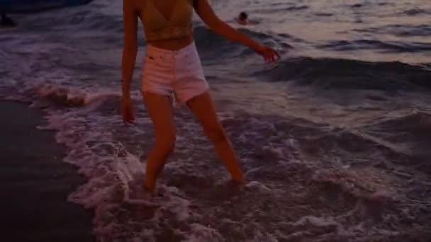 Νεαρή γυναίκα παίζει παφλασμό νερού σε τροπικό ωκεανό παραλία το βράδυ ηλιοβασίλεμα. Όμορφη σέξι ταιριάζει κορίτσι παιχνιδιάρικο στη θάλασσα κατά τη διάρκεια των ταξιδιωτικών διακοπών — Αρχείο Βίντεο