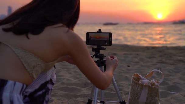 Young woman taking a photo of sunset beach sea view with her mobile phone . Female photographer using a tripod capture beautiful landscape pictures — Stock Video