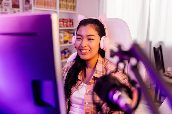 Opgewonden en lachende gamer meisje in schattige headset met mic spelen van een online video game. jonge aziatische vrouw praten met spelers en publiek op personal computer thuis — Stockfoto