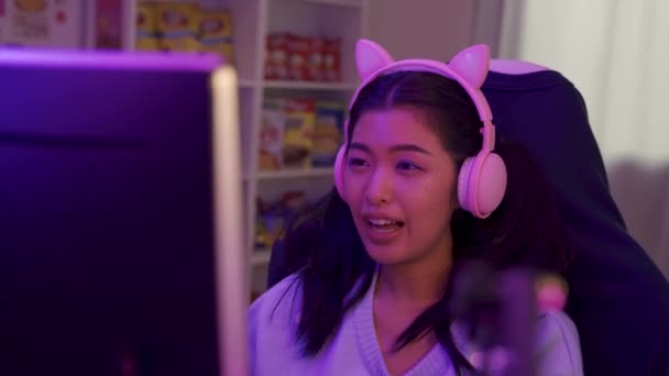 マイクをオンラインビデオゲームをプレイしてかわいいヘッドセットで興奮し、笑顔のゲーマーの女の子。若いアジアの女性は自宅で個人的なコンピュータ上の選手や観客と話して — ストック動画